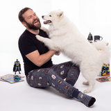 Man wearing Dark Knight sweatpants playing with a large white dog on a white background
