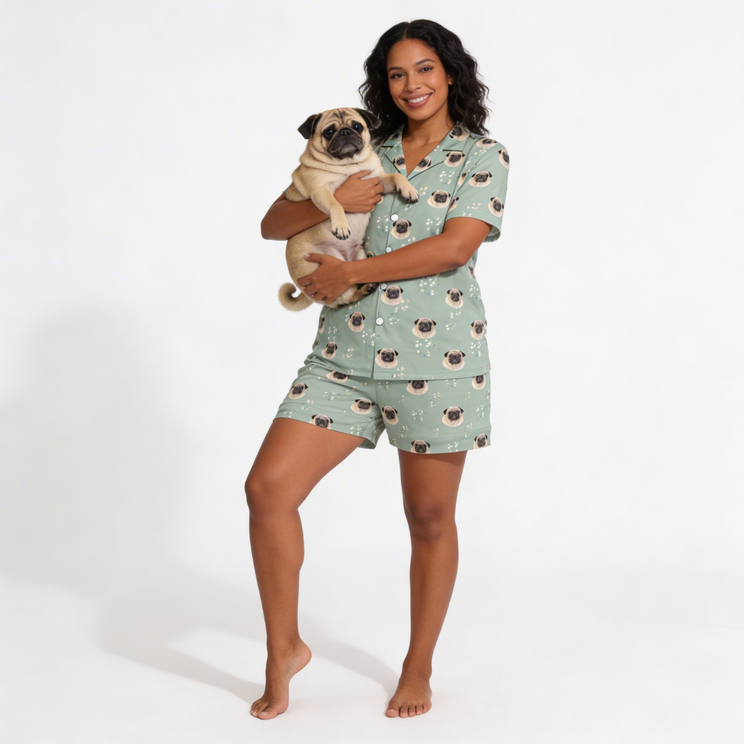 Woman wearing a green short button down pajama set with pug pattern, holding a pug dog on a white background[VintageBlooms]