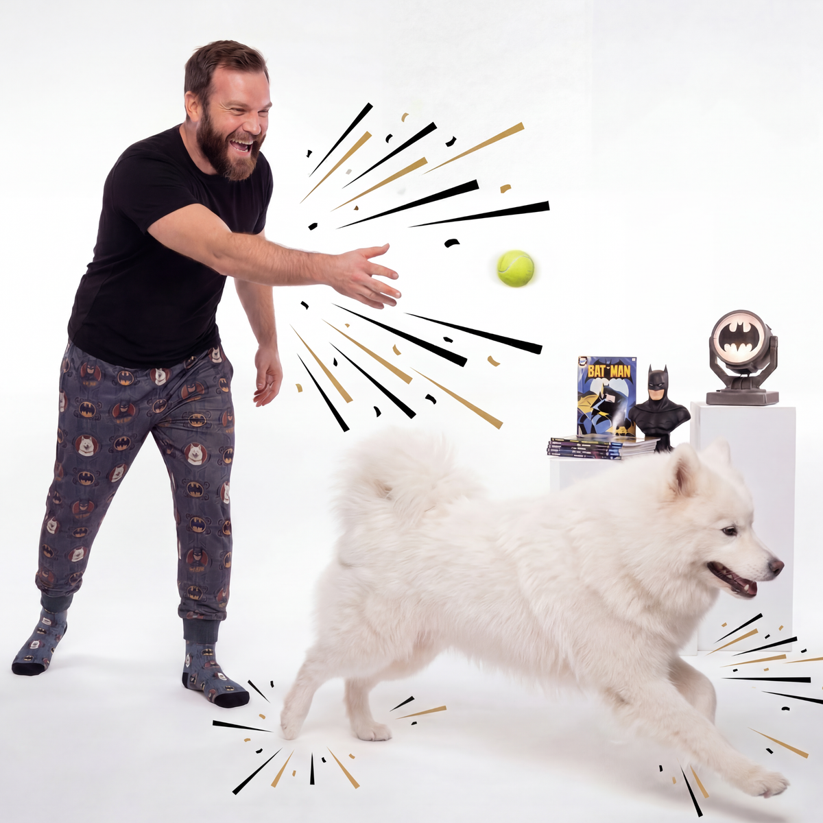 Man in pajama pants with Dark Knight Batman pattern interacting with a white dog on a white background