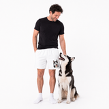 Man wearing white shorts with a dog graphic, standing next to a dog on a white background