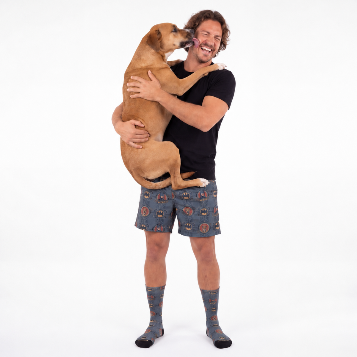 Man wearing a sweatshorts and socks holding a dog on a white background