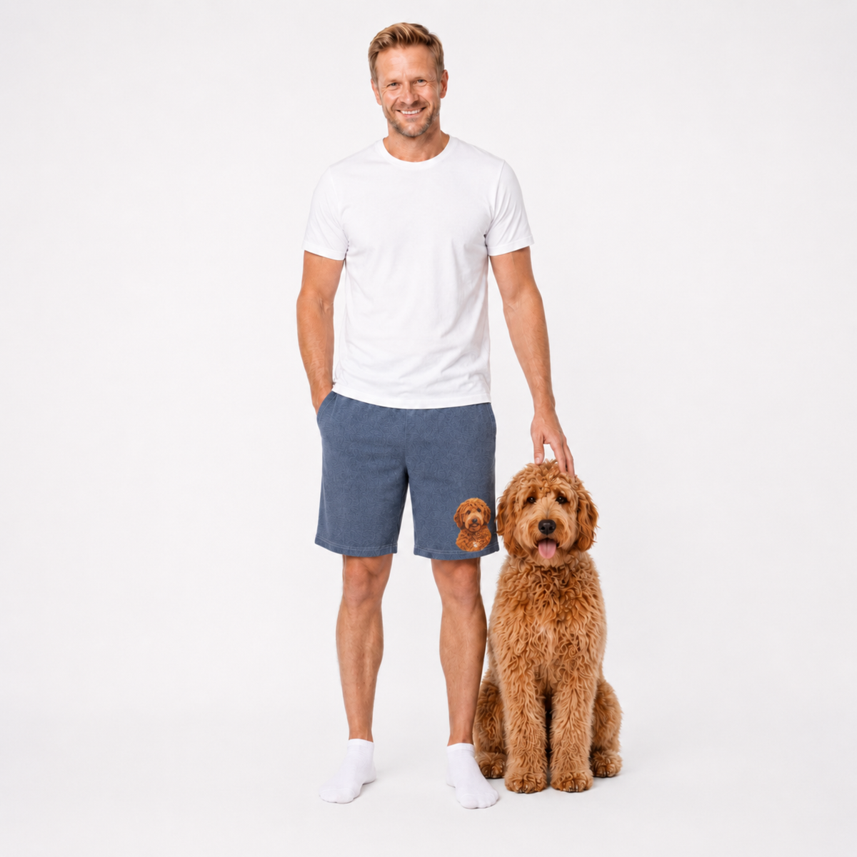 Man in white t-shirt and blue shorts standing next to a brown dog on a white background