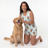 Woman in a dog-themed tank top pajamas kneeling next to a golden dog on a white background