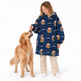 A woman wearing a navy blue hooded sweatshirt with a Christmas dog print is smiling and feeding a golden retriever dog on a white studio background.