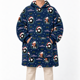 A person wearing a navy blue hooded robe with an all-over Christmas-themed print featuring penguin portraits, wreaths, snowflakes, and the text 'Christmas Vacation.' The robe has a front kangaroo pocket and hood, and the person is also wearing light beige pants against a plain light gray studio background.