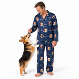 A man wearing navy blue pajamas with a Santa Claus and dog print stands barefoot on a white studio background while feeding a corgi dog.