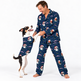 A man and a dog wearing matching navy blue pajamas with a Santa Claus and snowman print, posed against a clean white studio background.