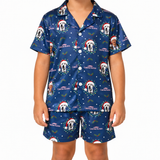 A child wearing a matching navy blue pajama set with a Christmas dog print. The set includes a short-sleeve button-up shirt and shorts, featuring white dogs in Santa hats, white text reading 'Merry Christmas Biker', and holiday decorations, shown against a plain white background.