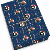 A rectangular gift box wrapped in navy blue Christmas-themed paper featuring repeated photos of a baby in Santa hats, with 'Merry Christmas' text, white snow dots, and green holly accents, tied with twine on a white background.