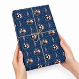 A person's hands holding a gift box wrapped in dark blue Christmas-themed paper with penguin illustrations, tied with a twine bow, against a plain white background.