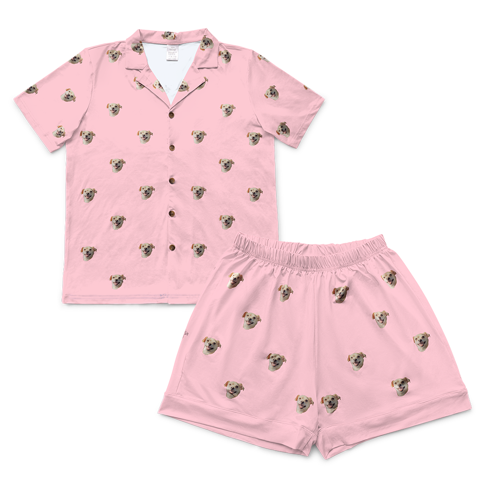 Pink pajama set with short-sleeved button-up shirt and matching shorts, featuring a scattered pattern of realistic small dog faces in tan and cream colors.