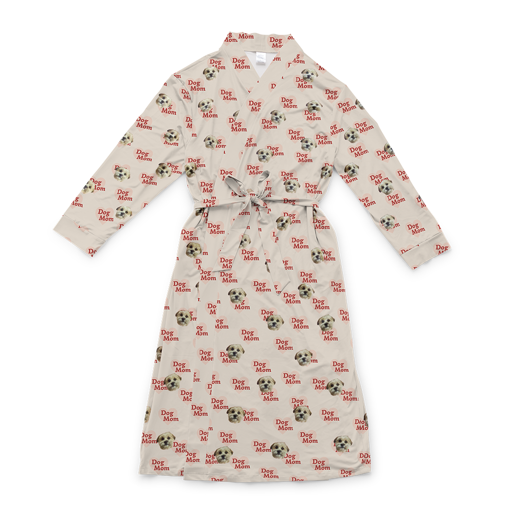 A light tan full-length robe with a tie belt, featuring a repeating custom pattern. The pattern includes several close-up photos of a small, light-colored dog's face, interspersed with graphics of reddish-brown hearts that contain the red text "Dog Mom". 