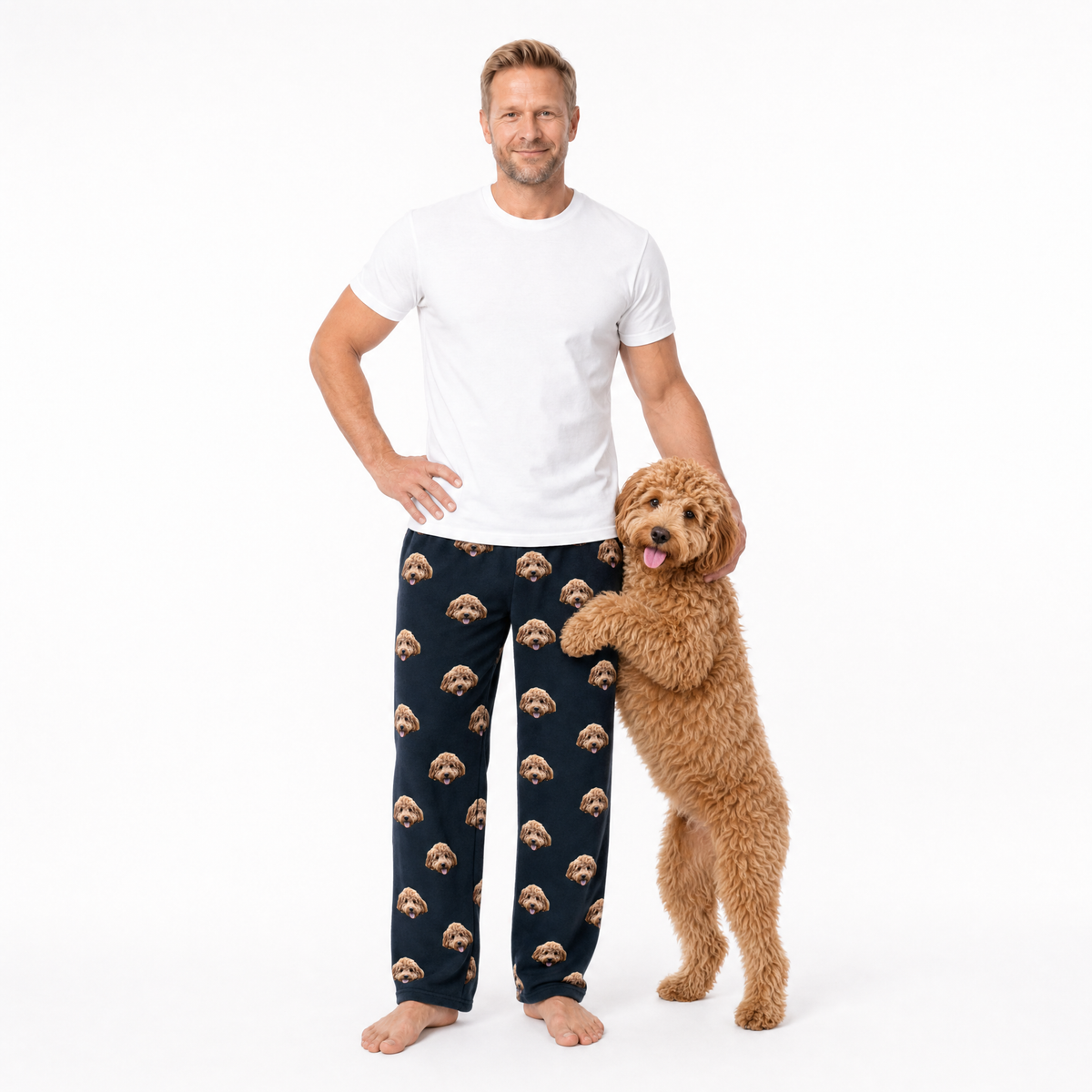 Man wearing black pajama pants with dog pattern standing next to a dog on a white background