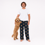 Man wearing black pajama pants with dog pattern standing next to a dog on a white background