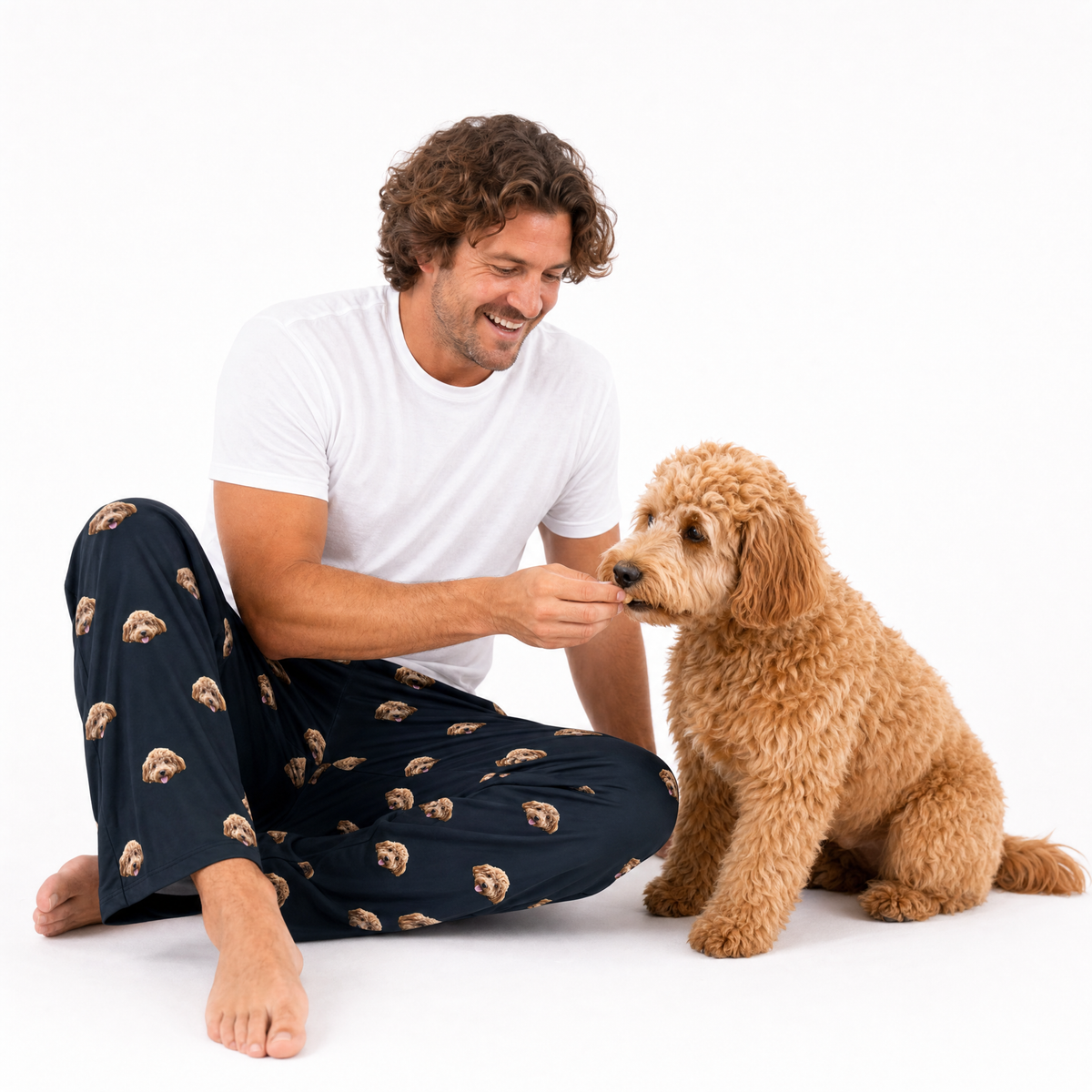 Man in black pajama pants with dog pattern sitting on the floor with a dog.