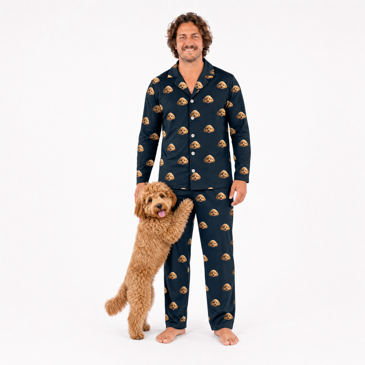 Man wearing black pajamas with dog pattern standing next to a dog on a white background