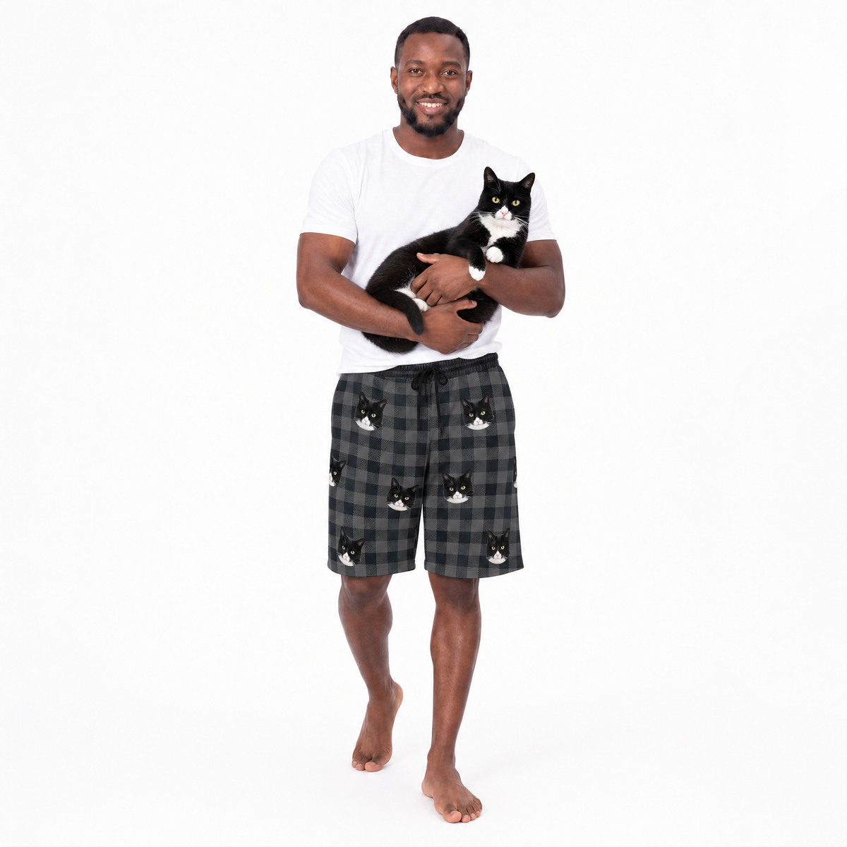 Man holding a cat wearing a white t-shirt and checkered shorts with cat designs on a white background