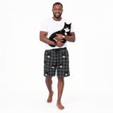 Man holding a cat wearing a white t-shirt and checkered shorts with cat designs on a white background