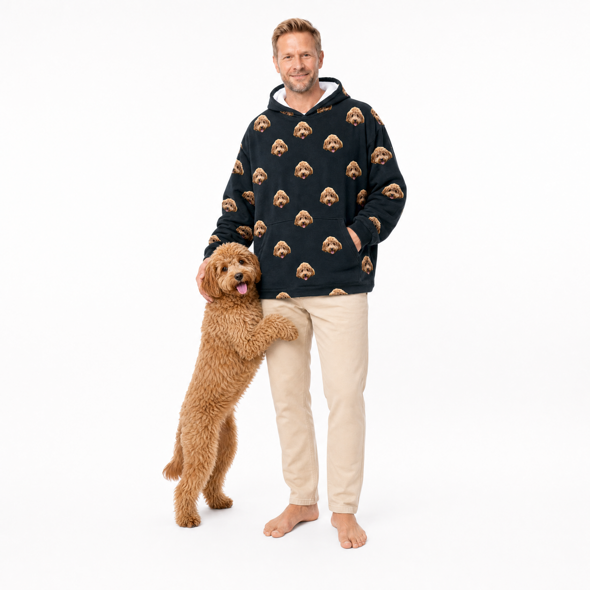Man wearing a black blanket hoodie with dog face patterns, standing next to a brown dog on a white background
