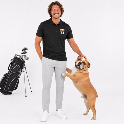 A man wearing a black polo shirt with a bulldog logo stands next to a brown bulldog dog, with a golf bag visible on the left, against a plain white studio background.