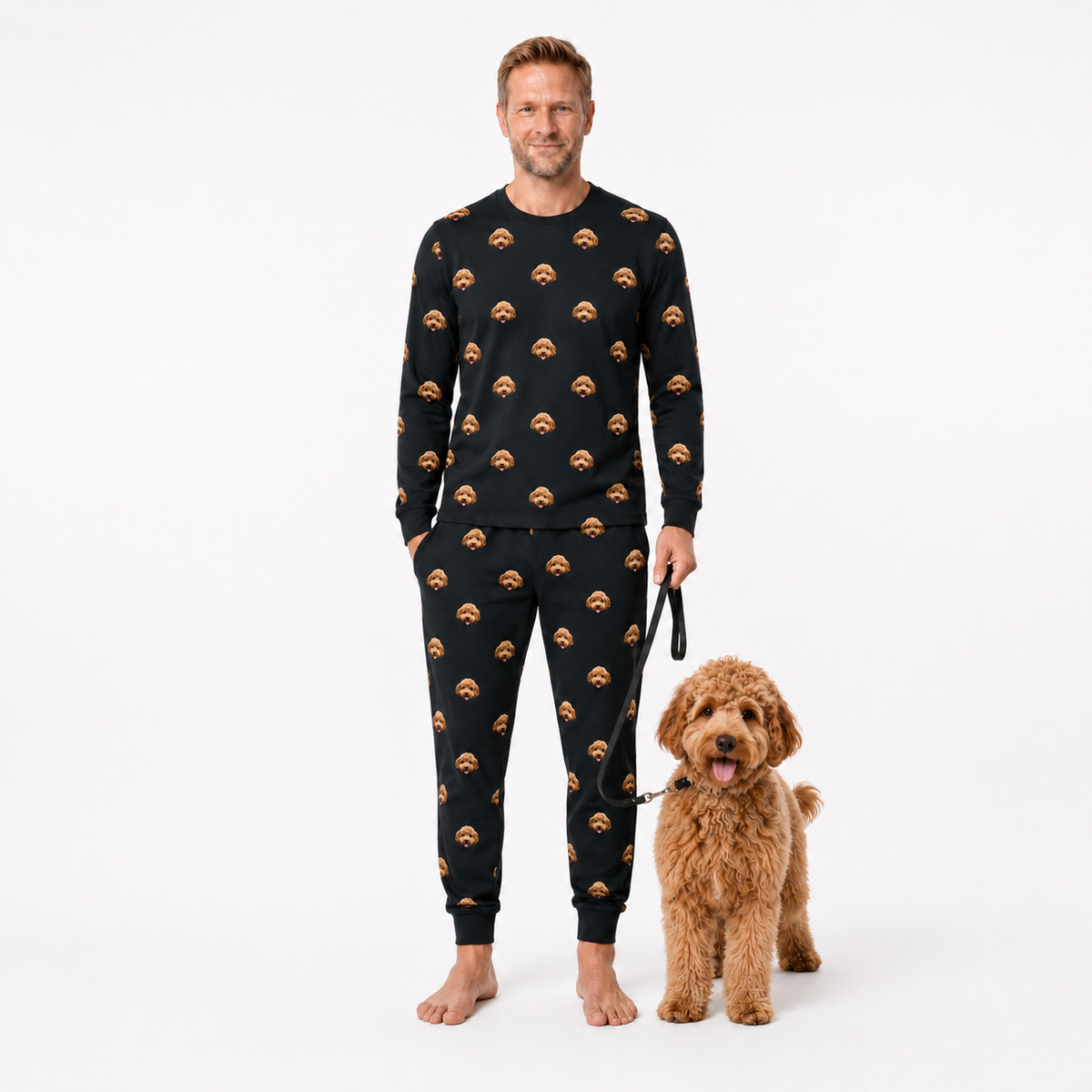 Man wearing a black jogger pajama set with a dog pattern, standing next to a brown dog on a white background.