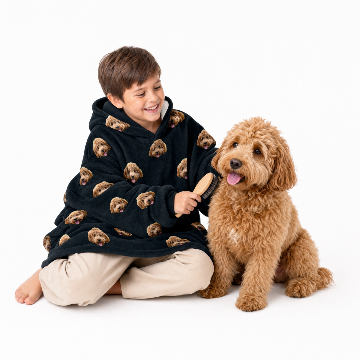 Child wearing a blanket hoodie with dog patterns, sitting with a dog on a white background