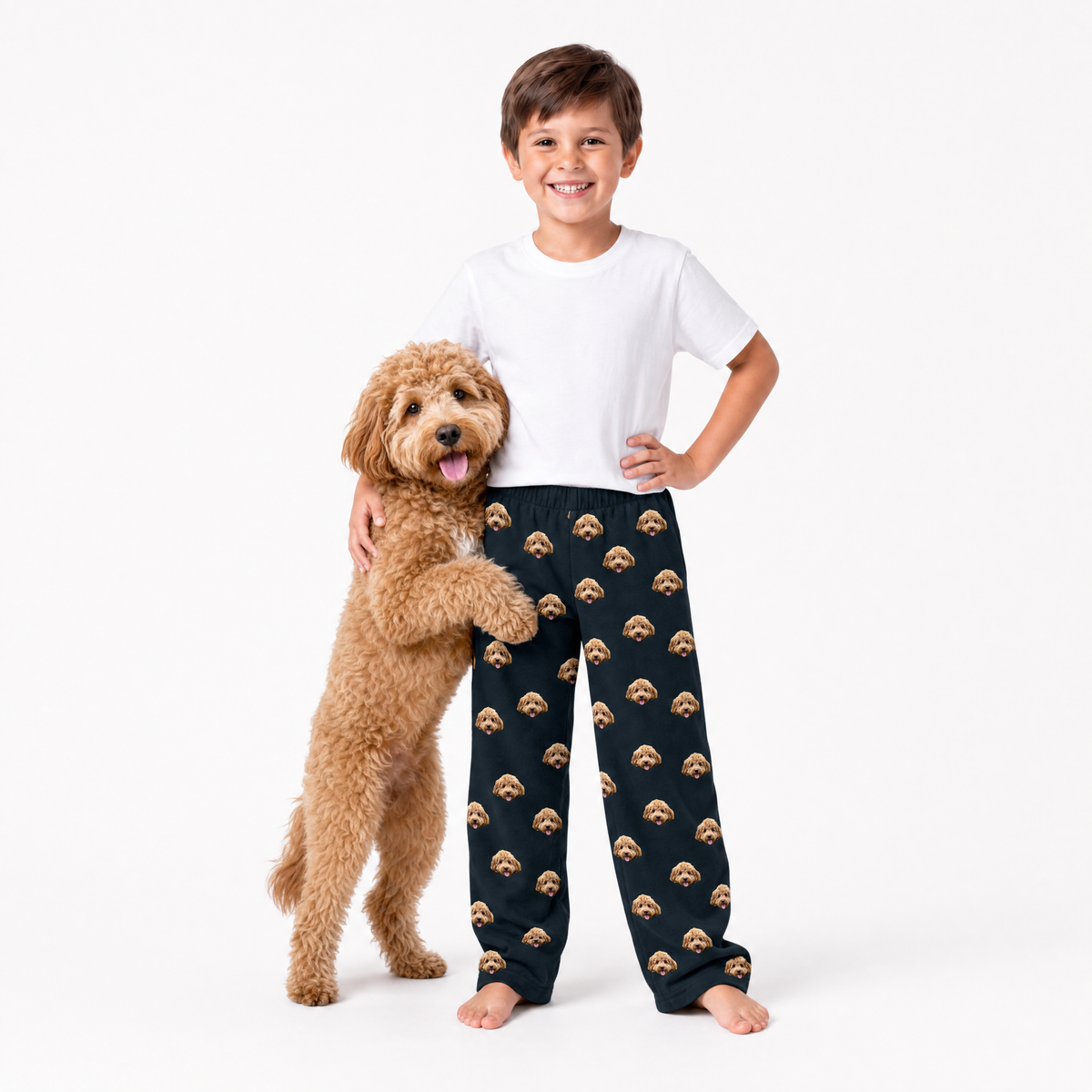 Child wearing black pajama pants with dog face pattern, standing next to a dog on a white background