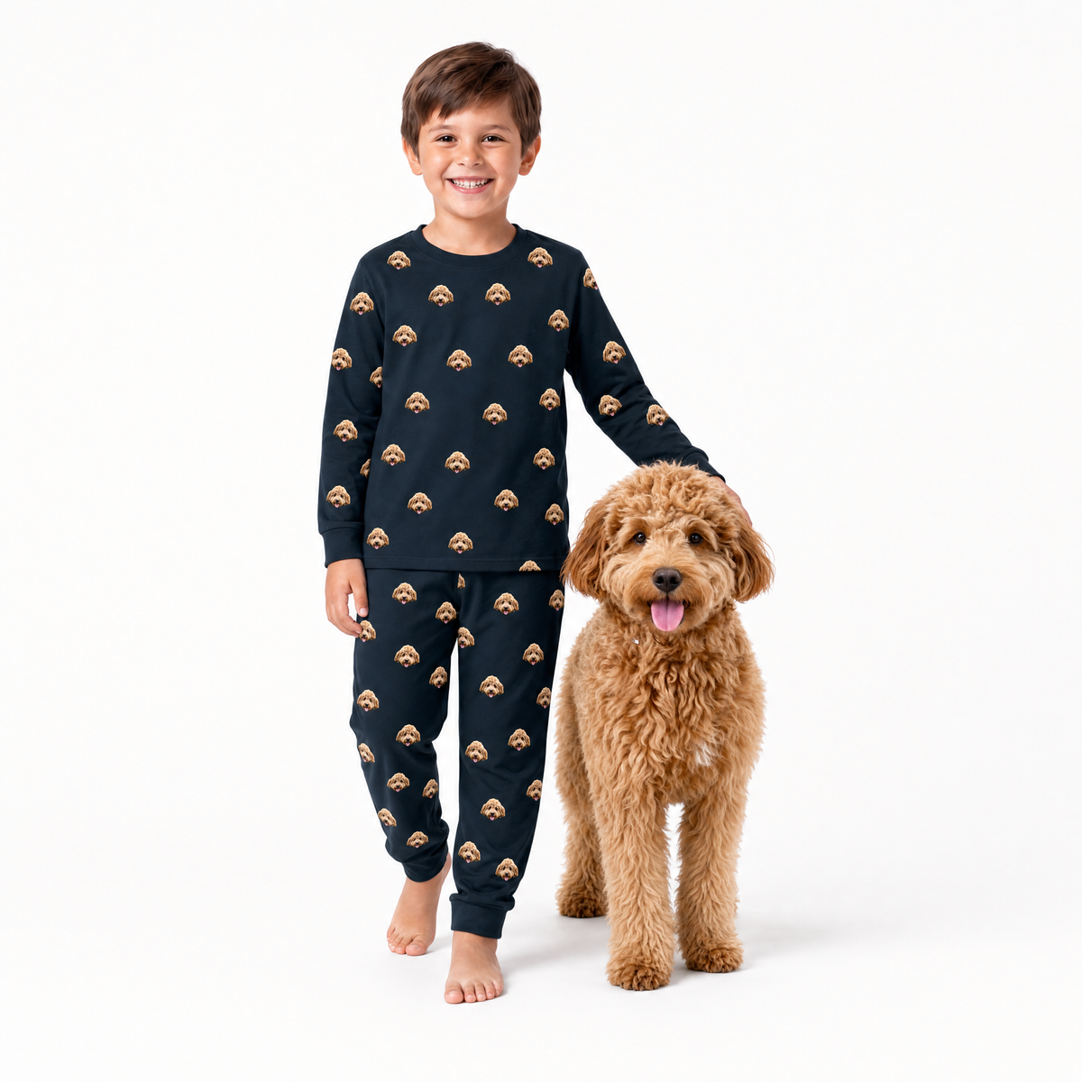 Child wearing black jogger pajamas with dog pattern standing next to a brown dog on a white background