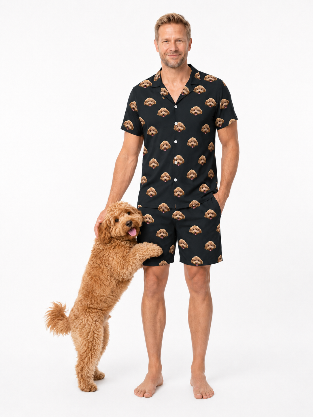 Man wearing a black patterned pajama set standing next to a dog on a white background