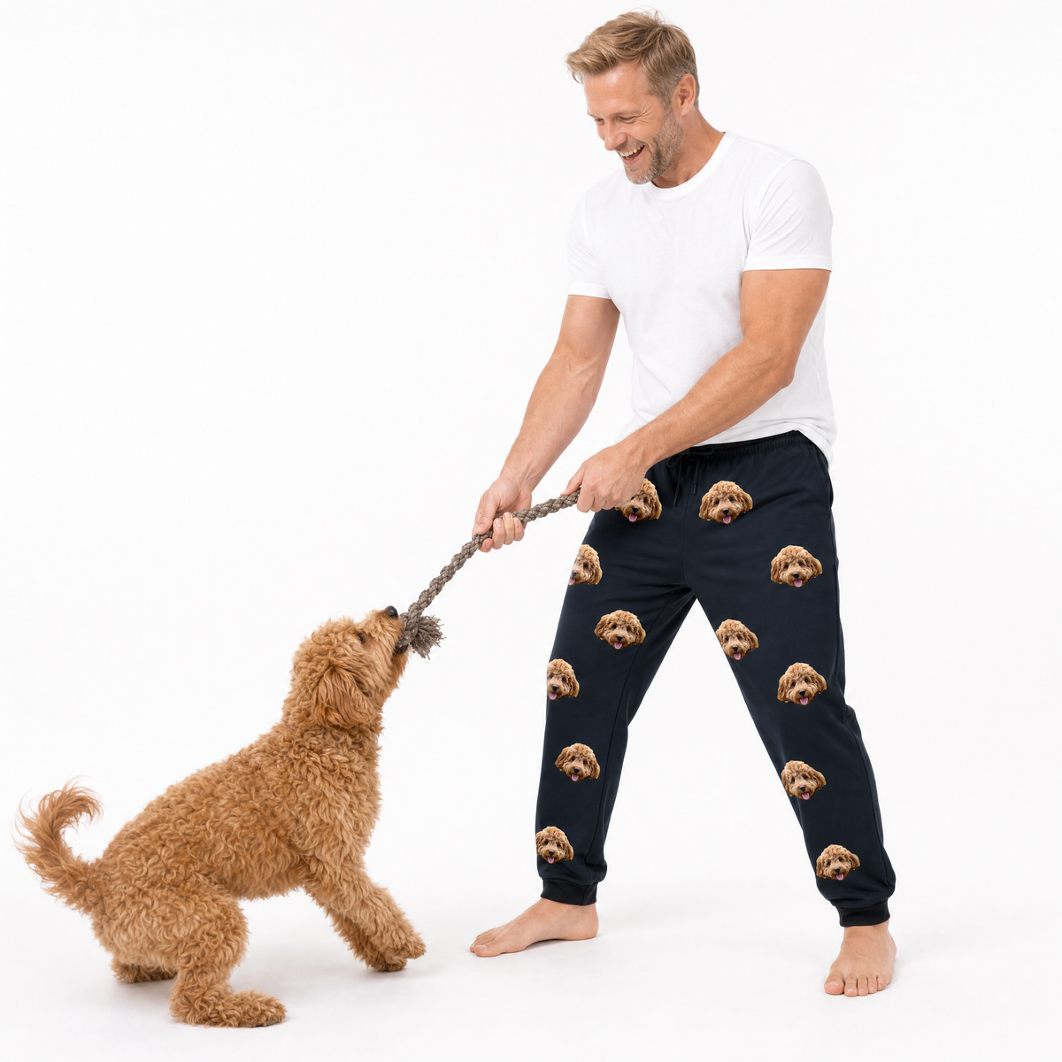 Man wearing navy jogger pants with dog pattern playing tug-of-war with a dog on a white background
