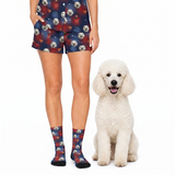 A person wearing matching navy pajama shorts and socks with a red and white dog print, standing beside a fluffy white poodle on a white studio background.