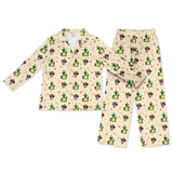 A two-piece long-sleeve pajama set featuring a collared top and matching pants, printed with a repeating pattern of cacti, campfires, candy canes, and small cartoon faces on a light cream background.