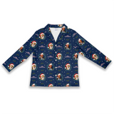 A long-sleeve button-front cardigan or pajama-style top in navy blue, featuring a repeating Christmas-themed print with a golden retriever wearing a Santa hat, green wreaths, snowflakes, and the word 'MERRY'.