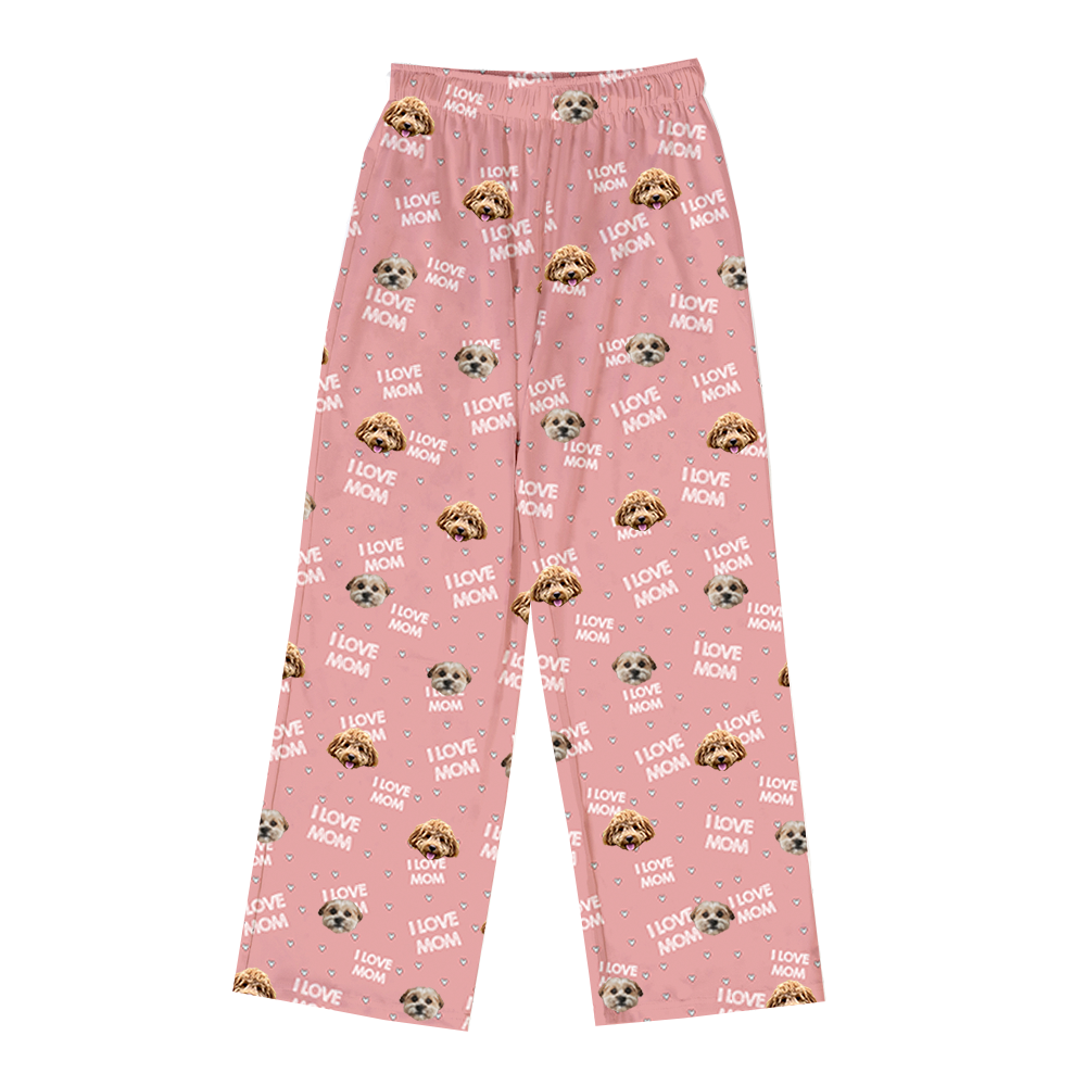 A pair of pink full-length pajama pants featuring a repeating pattern of two different light brown and white dog faces, and white text reading "I LOVE MOM" interspersed with small white hearts.