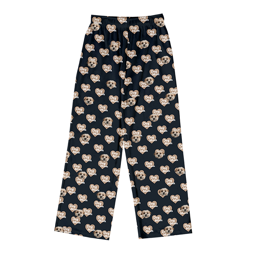 Black pajama pants covered in a repeating pattern. The pattern features alternating elements: light brown heart shapes with the text "Dog Mom" inside, and smiling headshots of a dog.