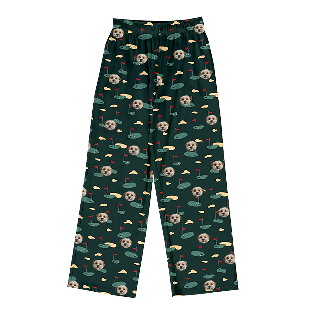 Dark green pajama pants covered in a repeating golf-themed pattern. The pattern features alternating elements: cartoon depictions of golf putting greens with a red flag, yellowish sand traps, and smiling headshots of a dog.