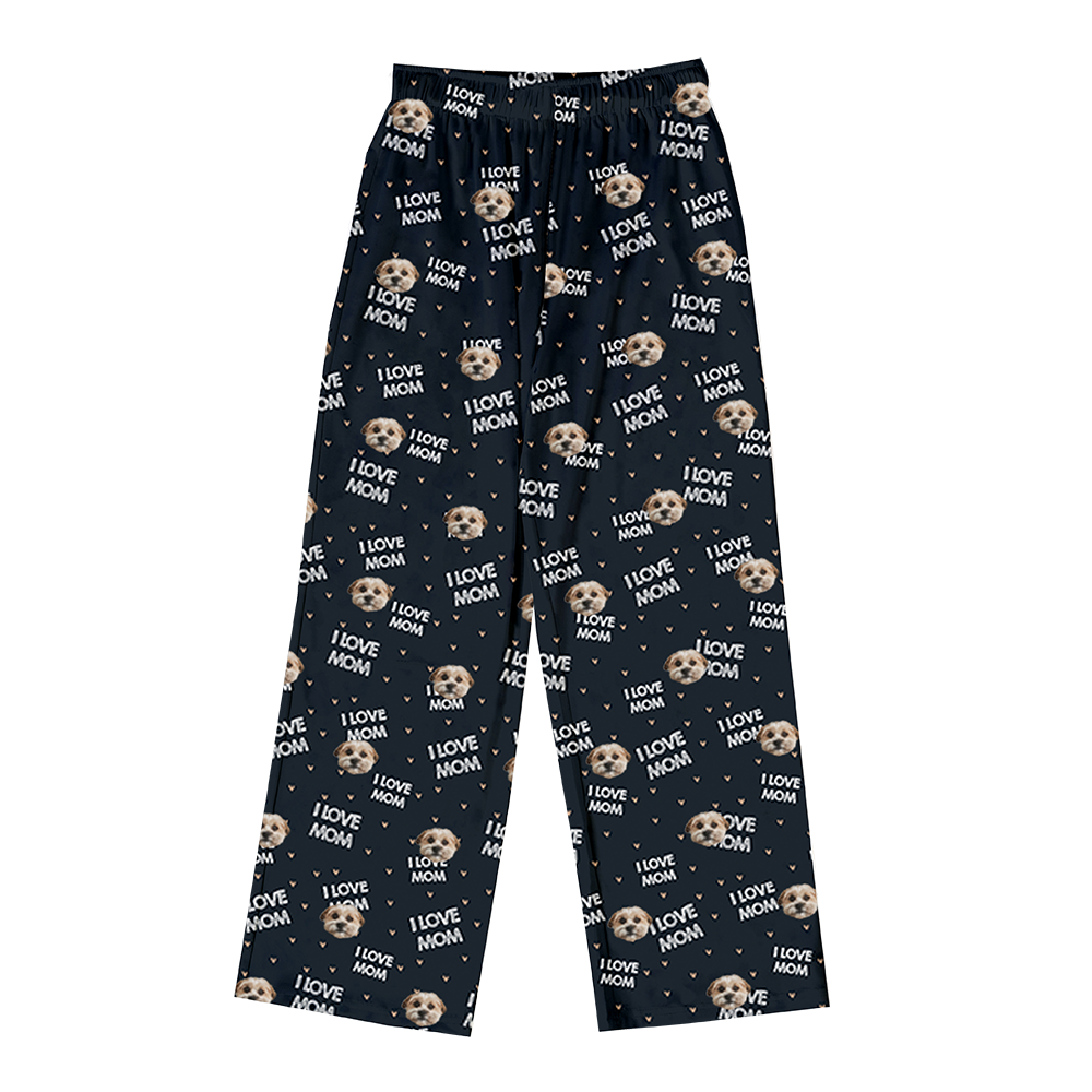 Black/dark navy pajama pants covered in a repeating pattern. The pattern features alternating elements: the phrase "I LOVE MOM" in light text, small golden heart icons, and smiling headshots of a dog.