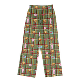 Green plaid lounge pants with a repeating pattern of golden retriever dog faces, pink silhouettes of people, and small colorful signs, shown flat against a white background.