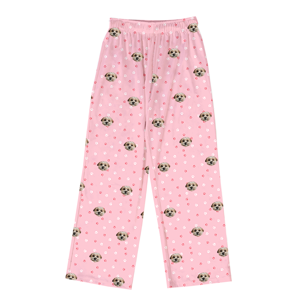 A pair of light pink, long pajama pants with an elastic waist. The pants feature a repeated pattern of small illustrations, including a light brown dog face.