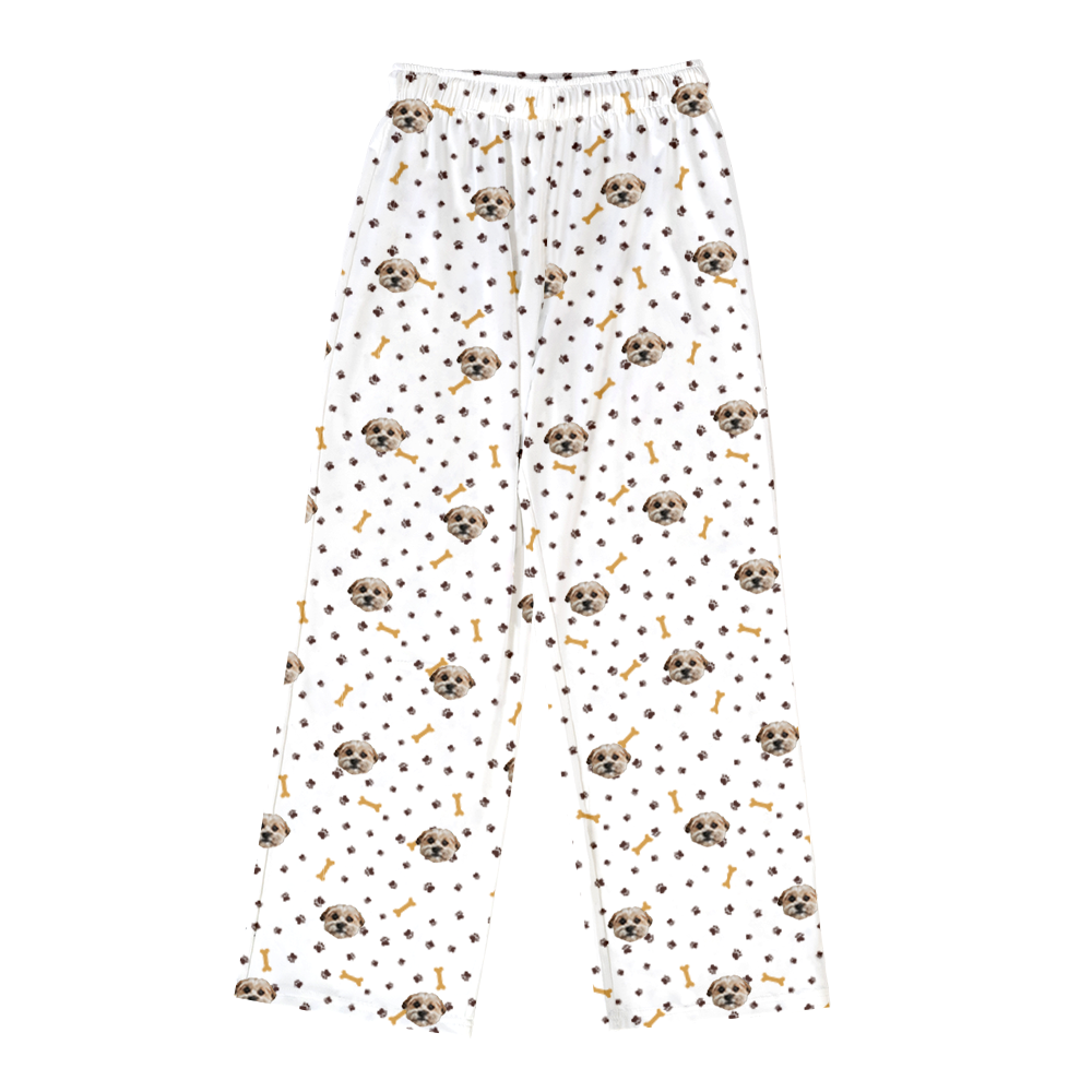White pajama pants featuring an all-over pattern of a small dog’s face, brown paw prints, and yellow dog bones.