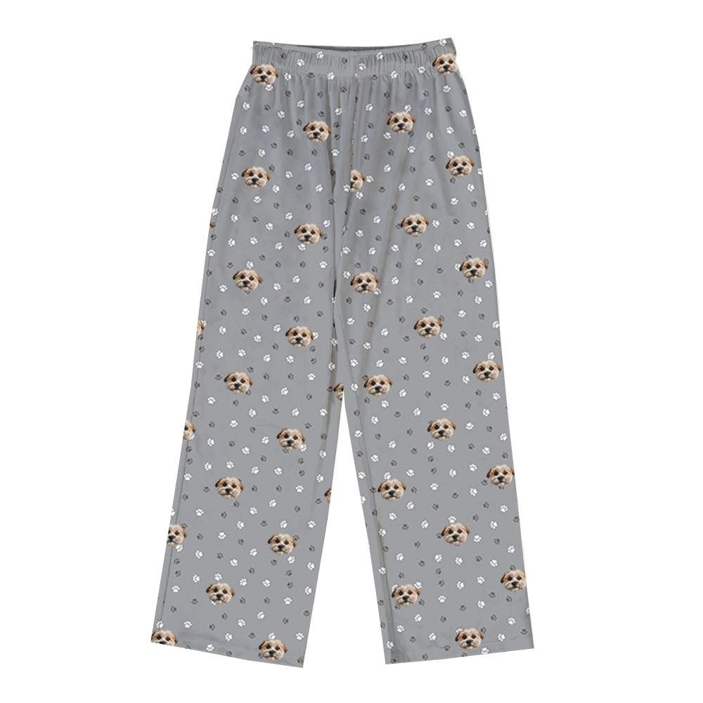 A pair of full-length pajama pants in slate grey with an elastic waistband. The pants feature a repeated pattern of small white and dark grey paw prints, interspersed with multiple images of a light brown and white dog's face.