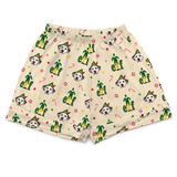 A pair of cream-colored boxer shorts featuring an all-over holiday print of Dalmatian dogs dressed as elves, candy canes, and the word 'elf' in green letters, with a matching elastic waistband.
