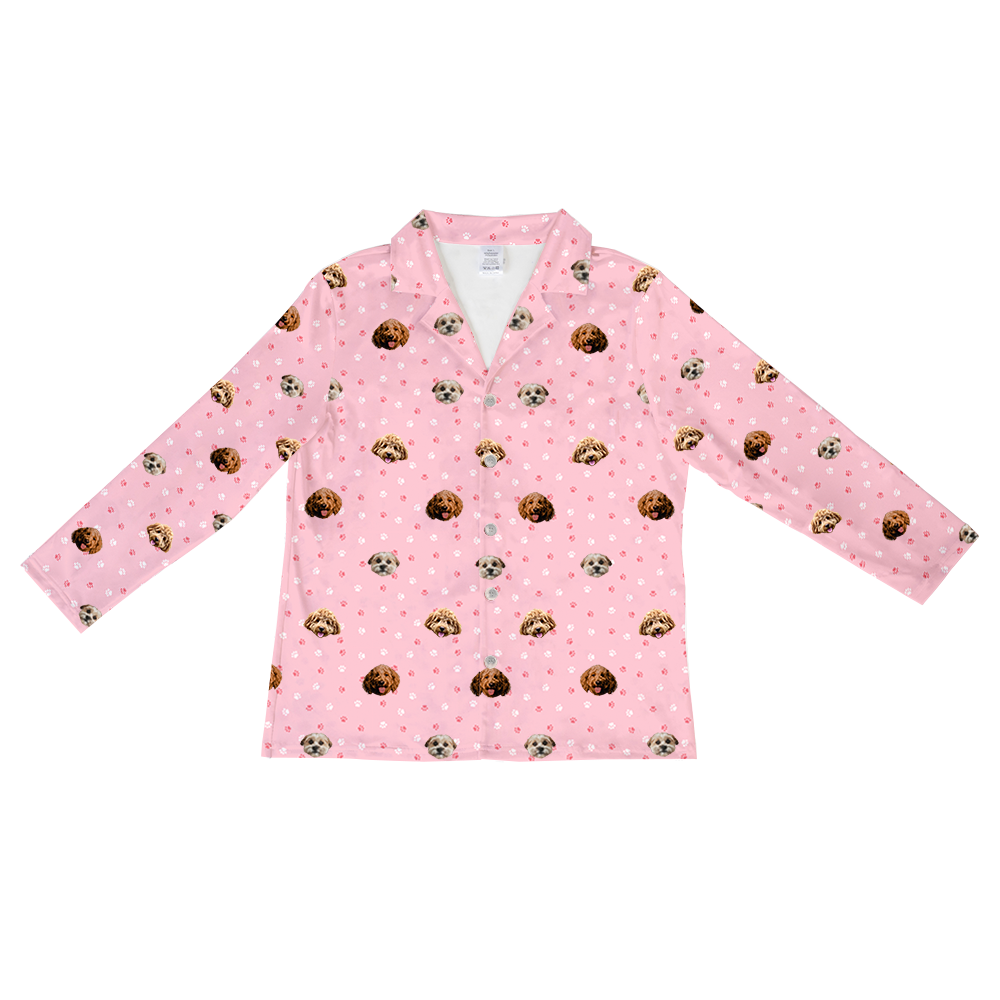 A light pink long-sleeve pajama top with a collar and button-down front, featuring a repeating pattern of white and dark pink paw prints, and small images of three different dogs' heads.