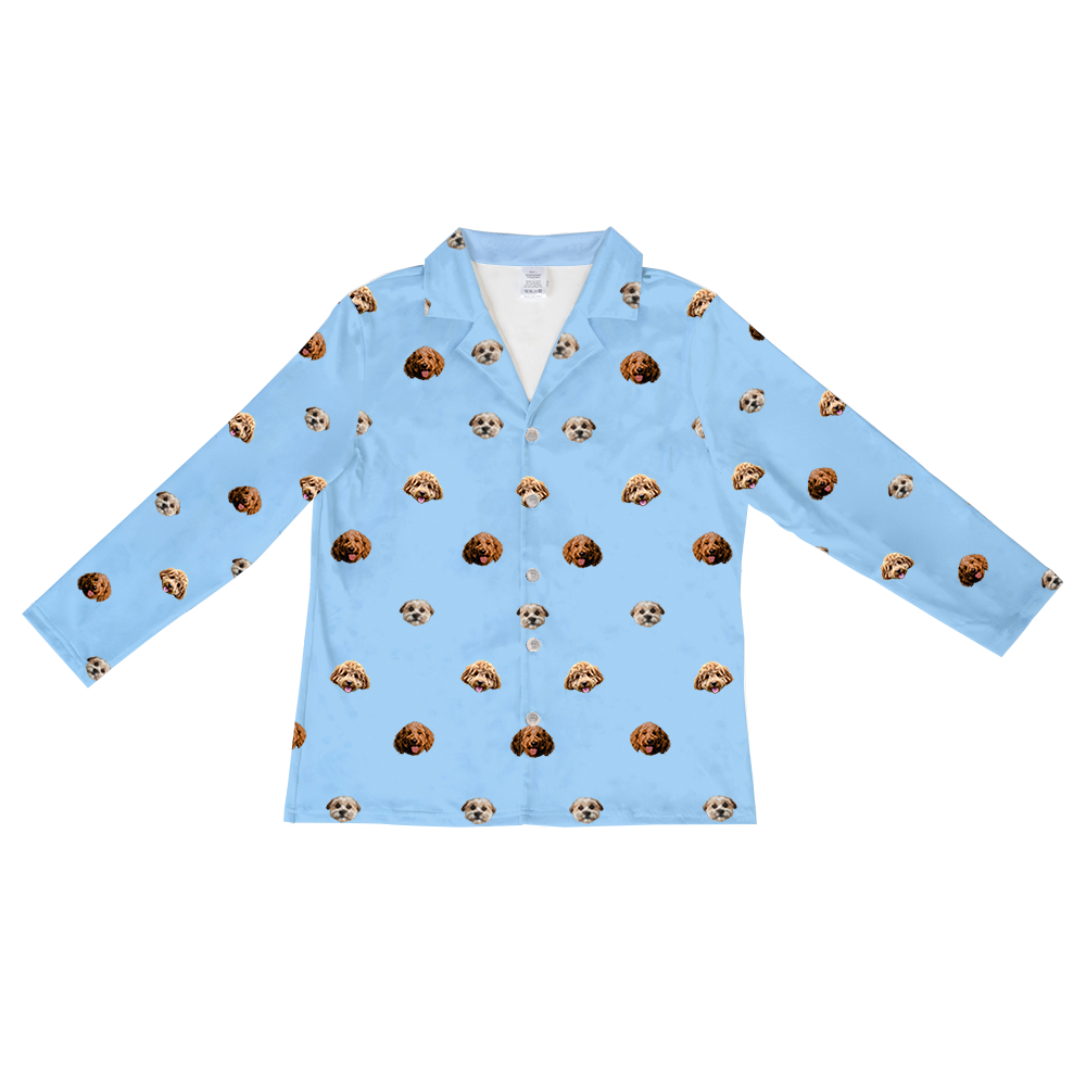 A sky blue, long-sleeved, button-down pajama top with a collared neck. The top features a repeated, scattered pattern of three different dog faces.