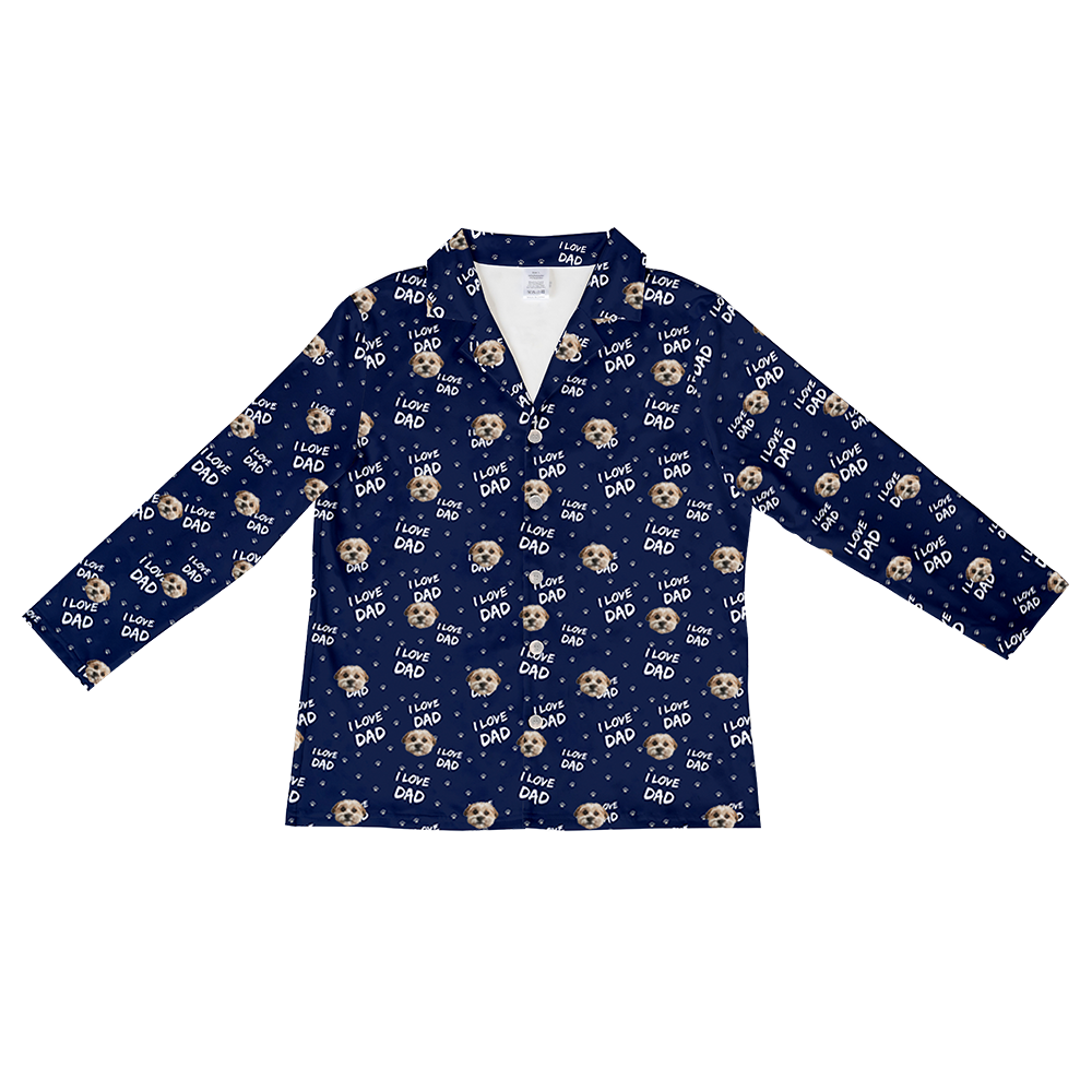 A long-sleeved, button-down pajama top in deep navy blue. The fabric features an all-over repeating pattern of small paws, small dog faces, and the text "I LOVE DAD" written in white script. 