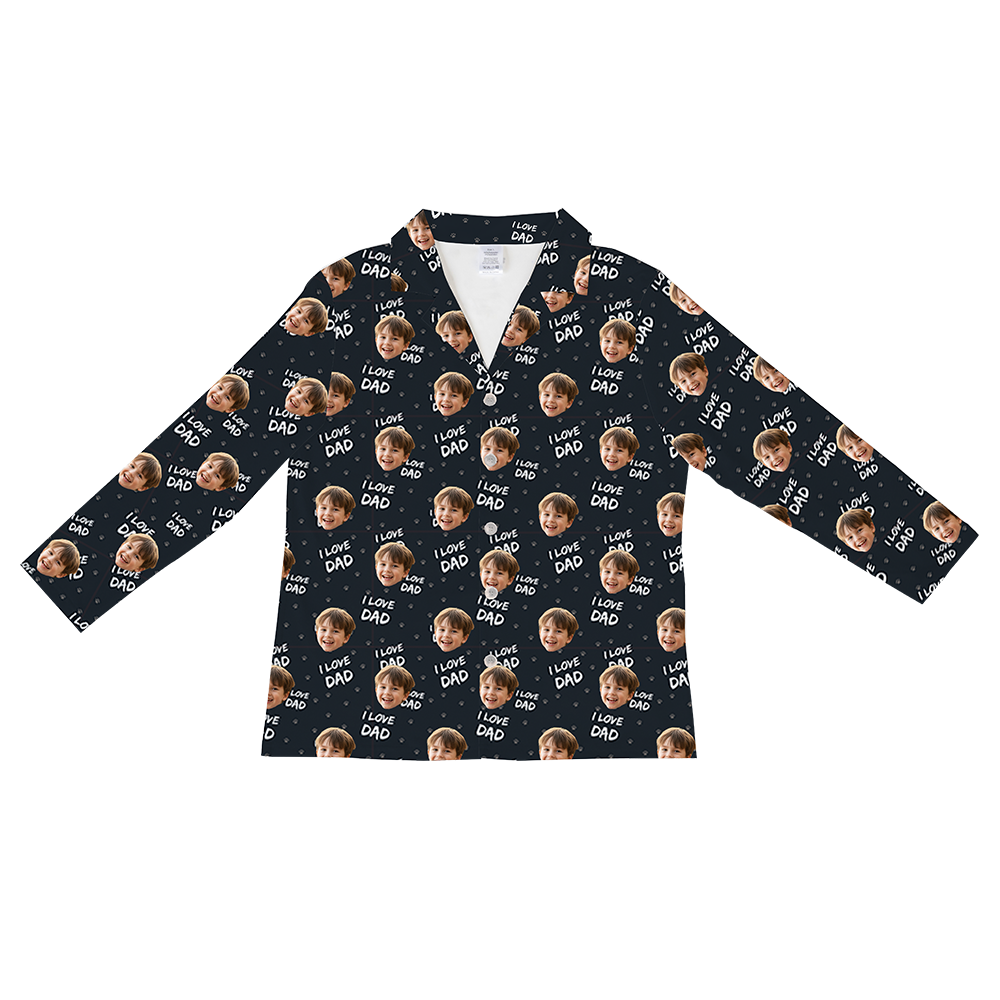 Long-sleeved, button-down pajama shirt in dark navy or black, patterned with repeating images of a young boy's smiling face, small hearts, and the white text 'I LOVE DAD'.