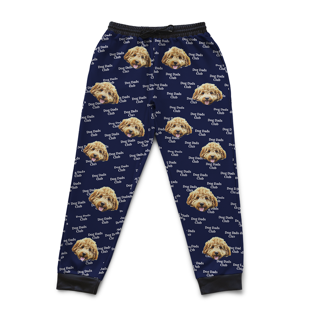Navy blue sweatpants patterned with repeated images of a fluffy tan dog’s face and the phrase ‘Dog Dads Club’ in white text.