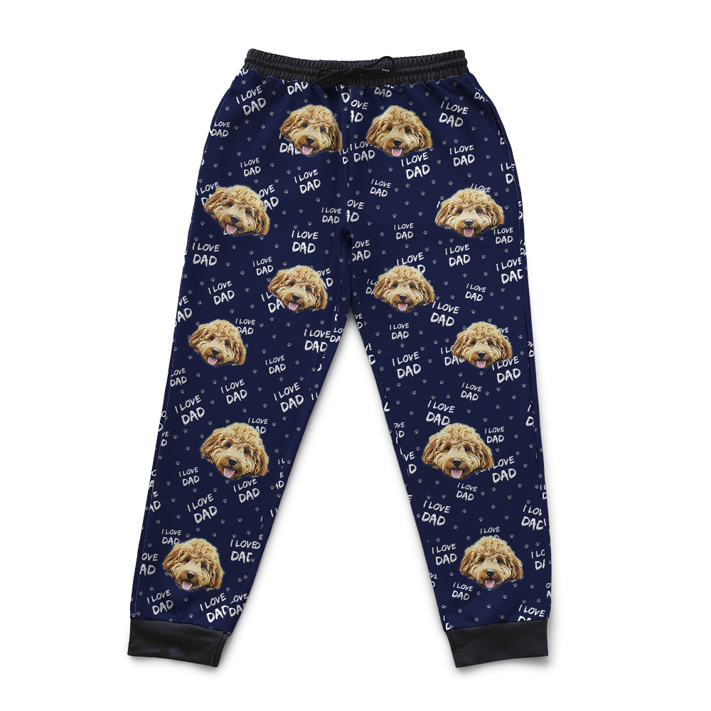 Navy blue jogger sweatpants featuring a repeating pattern of a fluffy light-brown dog’s face and the phrase ‘I Love Dad’ in white, with small paw print accents.