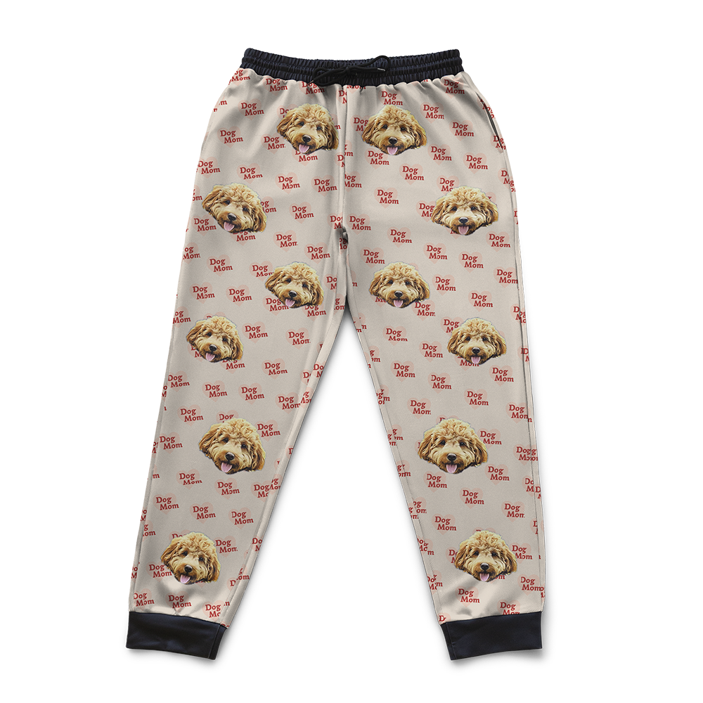Beige sweatpants with an all-over 'Dog Mom' pattern featuring repeated images of a fluffy light-brown dog’s face and red heart-shaped text.
