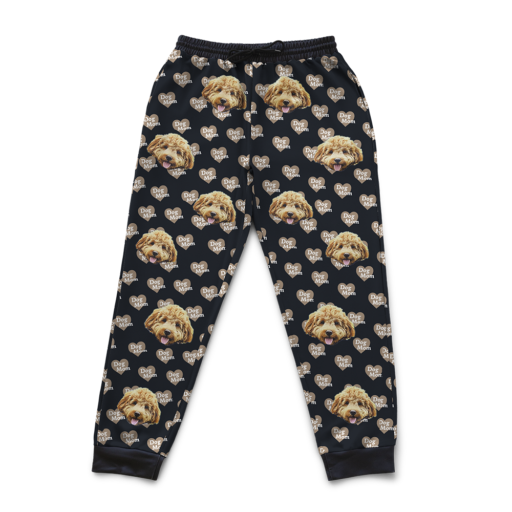 Custom sweatpants with a repeating pattern featuring a dog's face and beige heart-shaped “Dog Mom” icons on a black background.